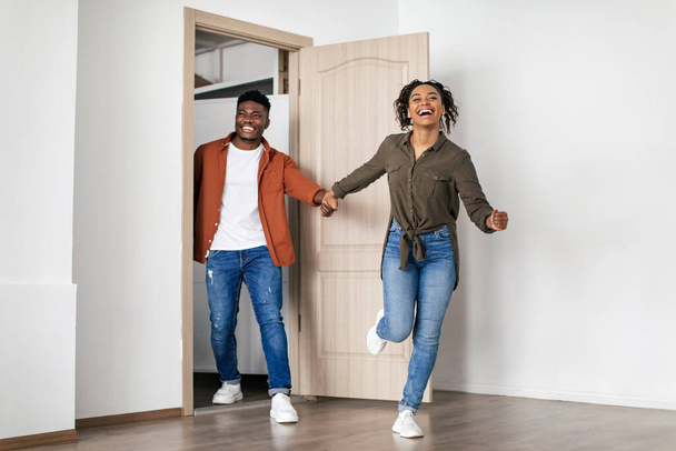 Щасливі покупці нерухомості. Захоплена афроамериканська пара біжить в кімнату, входячи в новий будинок. Дружина переїжджає додому. Повна довжина. Концепція оренди квартир і власності
 - Фото, зображення