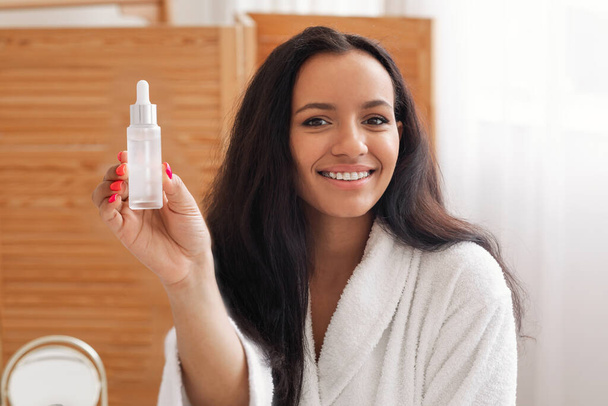 Pretty Woman Showing Cosmetic Bottle Recommending Serum Posing In Modern Bathroom At Home. Female Advertising Facial Skin Care Products Smiling To Camera Indoors. Skincare Concept - Fotoğraf, Görsel