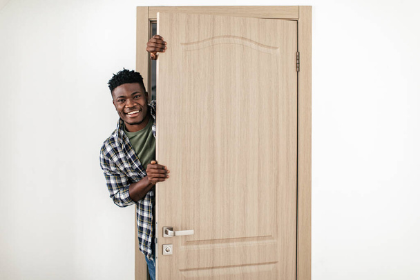 Positive Black Guy Smiling To Camera Opening Entry Door Of New House Standing Indoor. Young Man Posing In Opened Doors At Home. Real Estate Offer, Purchase And Rent Service - Foto, imagen