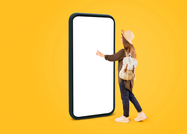 Vacation Offer. Tourist Woman Using Huge Cellphone With Empty Touchscreen Booking Travel Tickets Online Standing In Studio Over Yellow Background. Touristic App. Mockup - Fotoğraf, Görsel