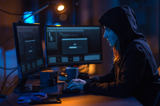 cybercrime, hacking and technology concept - female hacker in dark room writing code or using computer virus program for cyber attack - 写真・画像
