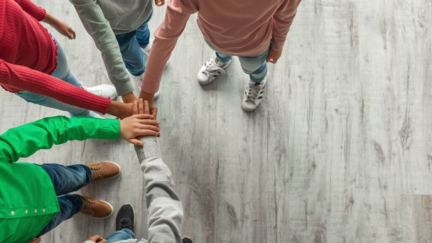 Teambuilding. Unrecognizable Kids Putting Hands Together Standing Indoors. Top View Shot Of Boys And Girls Stacking Arms. Teamwork And Unity Concept. Cropped, Panorama - 写真・画像