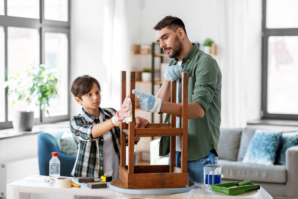 renovation, diy and home improvement concept - father and son degreasing old round wooden table surface with tissue - 写真・画像
