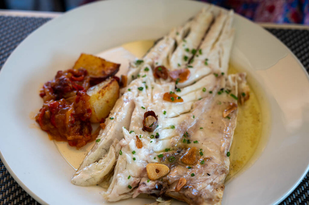 Essen im Restaurant von frischem Gegrilltem mit Knoblauch und Olivenöl auf alten Holzkohle parrillas weißen Wolfsbarsch Fisch in kleinen Fischerdorf Getaria, Baskenland, Spanien - Foto, Bild