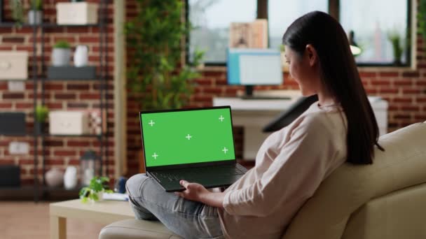 Young woman sitting at home with laptop having green screen chroma key display. Adult person sitting on sofa with portable computer on lap having mockup isolated template background. Tripod shot - Séquence, vidéo