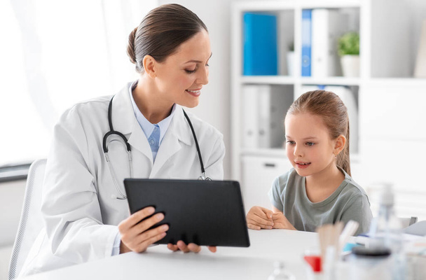 medicine, healthcare and pediatry concept - happy smiling female doctor or pediatrician showing tablet computer to little girl patient at clinic - Фото, зображення