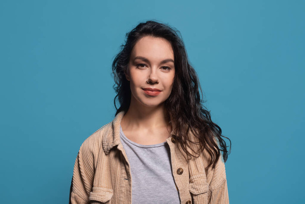 Portrait of smiling friendly pretty millennial caucasian brunette lady in casual, look at camera, isolated on blue background, studio. Student, blogger, advertisement and offer and facial expression - Фото, изображение