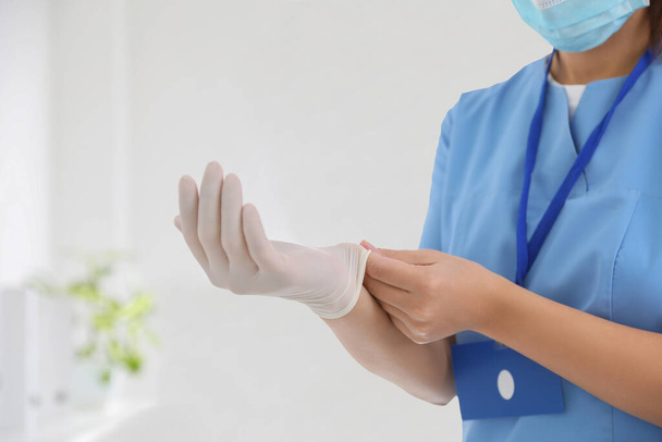Doctor putting on medical gloves against blurred background, closeup - Valokuva, kuva