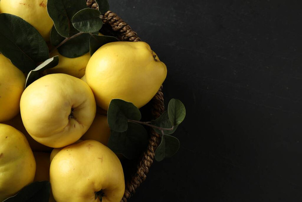 Fresh ripe organic quinces with leaves in wicker basket on black table, closeup. Space for text - Foto, Imagem