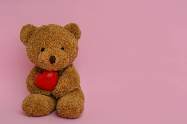Cute teddy bear with red heart on pink background, space for text. Valentine's day celebration - 写真・画像