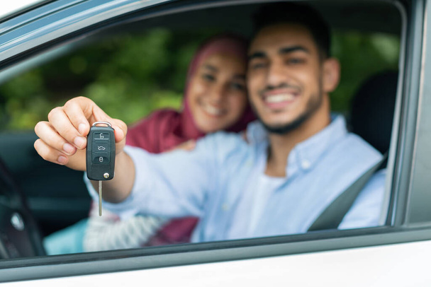 Test drive transport. Glad happy millennial arab woman in hijab and man show keys from new car, enjoy to purchase, couple have fun together, blurred. Buying own auto, credit, ad and offer, copy space - Photo, image