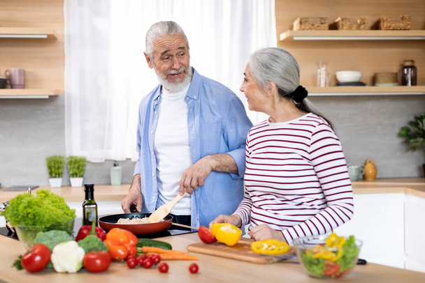 Happy Elderly Spouses Cooking Lunch Meal Together In Kitchen, Married Senior Couple Chatting While Preparing Healthy Food At Home, Old Man And Woman Enjoying Pastime On Retirement, Free Space - Foto, afbeelding