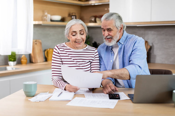 Financial Planning On Retirement. Portrait Of Happy Senior Couple With Laptop And Papers In Kitchen Discussing Family Budget Together, Elderly Spouses Calculating Spends And Taxes, Closeup Shot - Fotó, kép