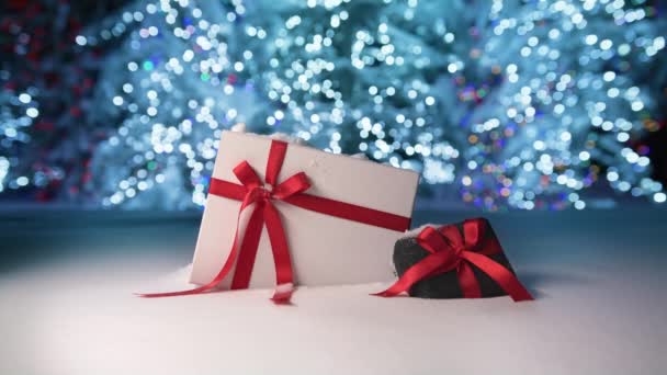 Magic night on Christmas eve with beautiful elegant gift boxes decorated with satin red ribbons. White and velvet black box on snow surface and glowing blue lights trees on blurry background, RED shot - Metraje, vídeo