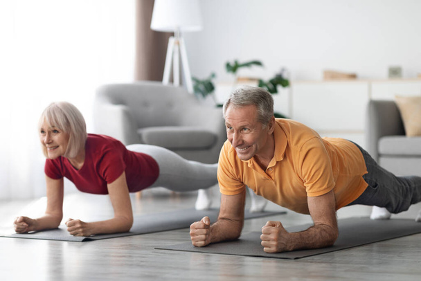 Cheerful athletic mature couple having workout at home, senior man and woman in sportswear exercising together, planking, looking at copy space and smiling, full length shot. Sport for seniors - Fotó, kép