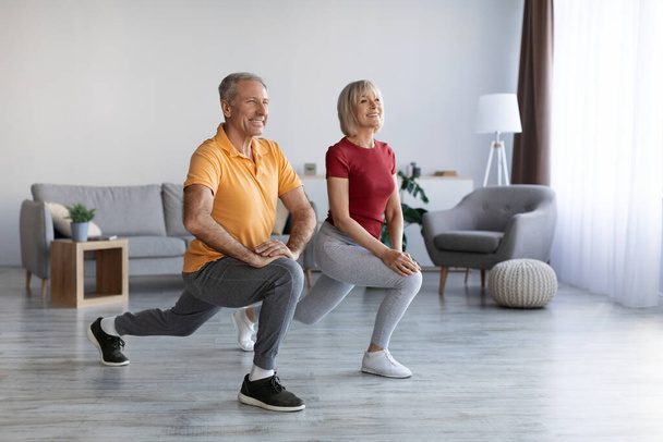 Positive beautiful mature couple having workout at home, cheerful senior man and woman in sportswear exercising together, looking at copy space and smiling, full length shot. Sport for seniors - Foto, Imagen