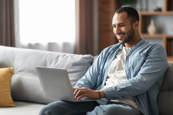 Remote Work. Handsome Young Black Freelancer Guy Using Laptop At Home, Smiling African American Male Working Online On Computer While Sitting On Comfortable Couch In Living Room, Copy Space - Fotografie, Obrázek