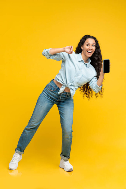 Great Application. Happy Middle Eastern Woman Showing Cellphone With Empty Screen Advertising Mobile App Standing Over Yellow Background. Vertical, Studio Shot - Foto, Imagem