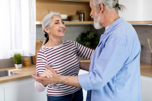 Portrait Of Loving Senior Couple Dancing Together In Kitchen Interior, Happy Romantic Elderly Spouses Having Fun, Holding Hands And Smiling To Each Other, Enjoying Spending Time At Home, Closeup Shot - 写真・画像