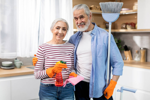 Domestic Chores Concept. Happy Senior Spouses Posing With Cleaning Supplies In Kitchen Interior, Beautiful Elderly Husband And Wife Smiling At Camera, Mature Couple Ready To Wash Home, Copy Space - Fotó, kép