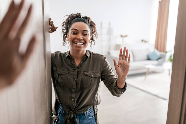 Hello. Happy African American Lady Waving Hello Opening Door Of Apartment Meeting Friend Standing At Home. Female Real Estate Owner Gesturing Hi. Selective Focus - Photo, image