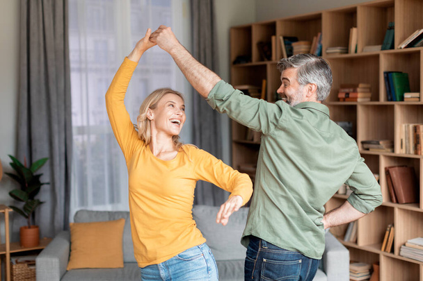 Portrait Of Positive Middle Aged Couple Dancing In Living Room Interior, Cheerful Mature Husband And Wife Having Fun At Home, Joyful Man And Woman Enjoying Spending Time Together, Free Space - Photo, image