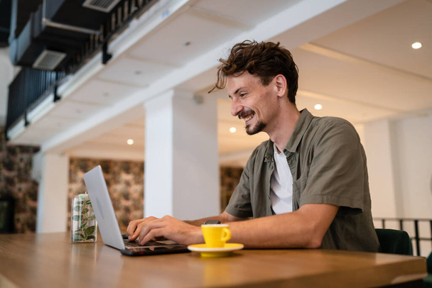 One adult modern man caucasian male with beard and mustaches wear causal shirt working remote from cafe freelance work or blog checking online content or browsing internet while sitting alone - Фото, изображение