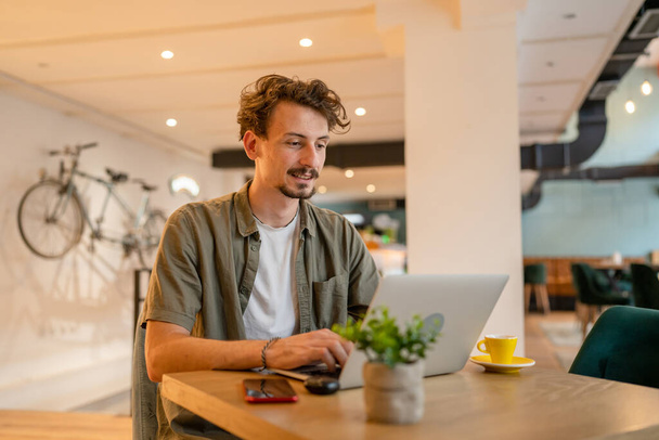 One adult modern man caucasian male with beard and mustaches wear causal shirt working remote from cafe freelance work or blog checking online content or browsing internet while sitting alone - Foto, Bild