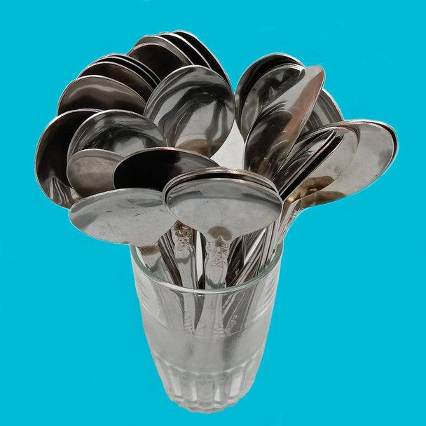 A number of tablespoons that have been used are arranged into one glass cup, plain background - Foto, Bild