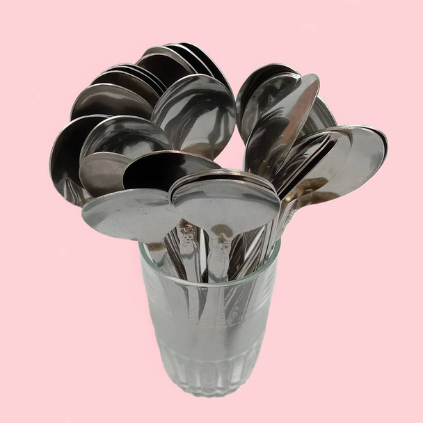 A number of tablespoons that have been used are arranged into one glass cup, plain pink background - Fotografie, Obrázek