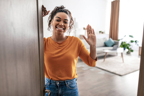 Joyful African American Lady Waving Hello Smililng To Camera Opening Entry Door At Home. Female Gesturing Hi Posing Indoors. Real Estate Property Purchase Concept - Photo, image