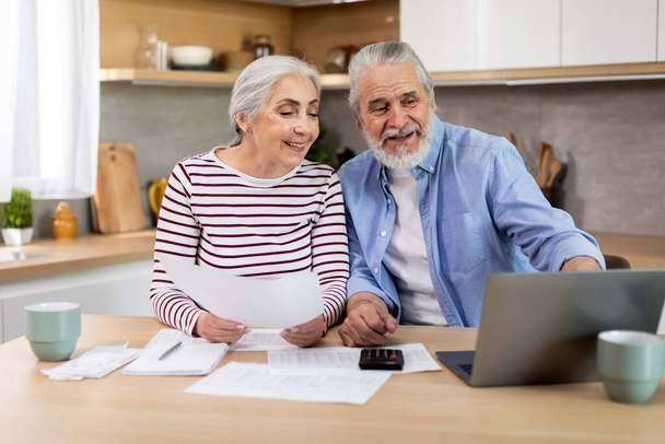 Happy Senior Spouses Making Family Budget Planning In Kitchen, Cheerful Elderly Couple Using Laptop And Checking Financial Papers Together, Doing Utility Payments In Internet, Closeup Shot - Photo, Image