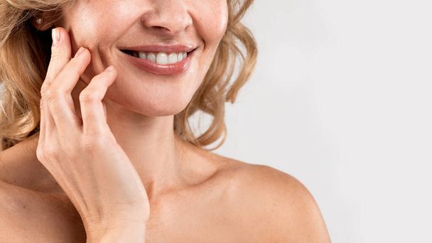 Anti-Age Treatments. Cropped Shot Of Smiling Middle Aged Woman With Beautiful Skin And Bare Shoulders Standing Over Light Gray Studio Background, Attractive Mature Female Touching Face, Panorama - Photo, Image