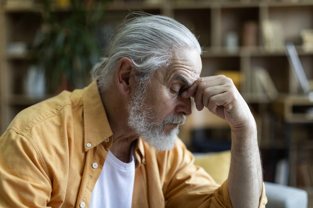 Side view of sad bearded elderly man touching his nose bridge, experiencing financial hangover while crisis 2022, closeup shot, copy space. Financial topics and resources for seniors - Photo, image