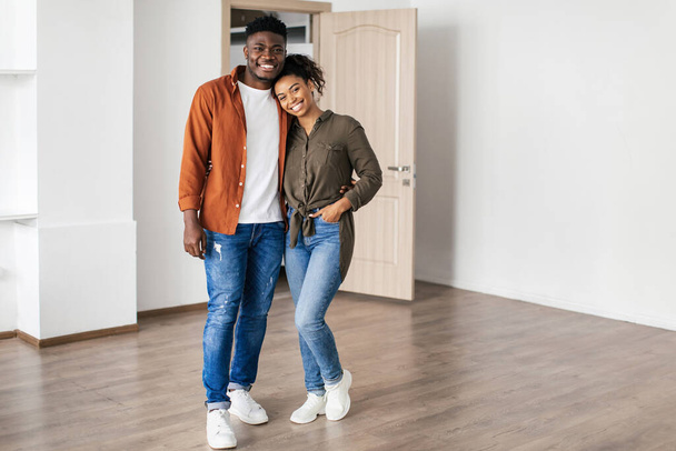 Real Estate. Happy Married Couple Posing Embracing In Empty Living Room In New House Indoor After Relocation. Spouses Standing In Rented Apartment. Property Purchase Concept - Zdjęcie, obraz