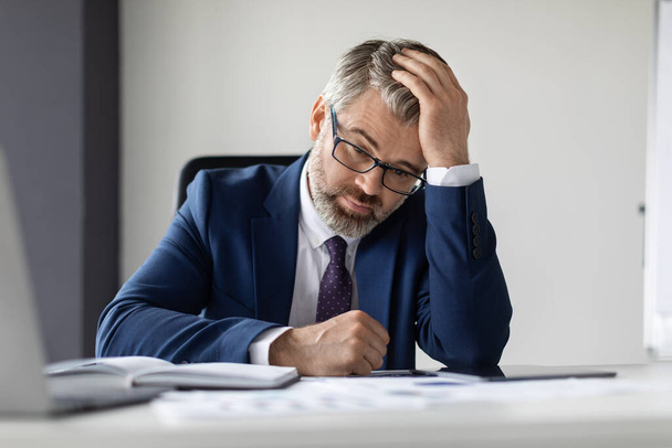 Work Burnout. Portrait Of Upset Mature Businessman Sitting At Desk In Office, Pensive Middle Aged Male Entrepreneur In Suit Touching Head, Suffering Depression Or Business Failure, Closeup Shot - Zdjęcie, obraz