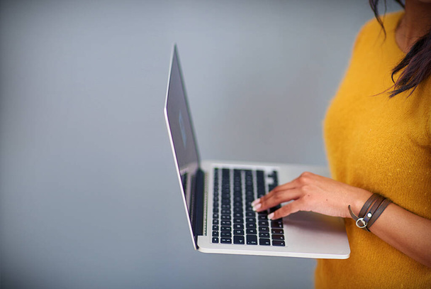 Life online. Cropped studio shot of a woman using a laptop against a gray background - Foto, imagen