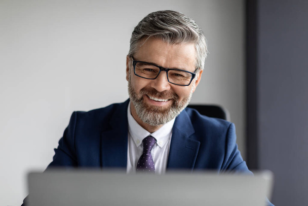 Closeup Portrait Of Handsome Bearded Middle Aged Businessman Wearing Eyeglasses Working With Laptop In Office, Smiling Happy Male Entrepreneur In Suit Using Computer At Workplace, Copy Space - Photo, Image