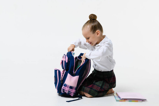 Cute girl in school uniform collects a backpack for classes Isolated on a white background. - Foto, afbeelding