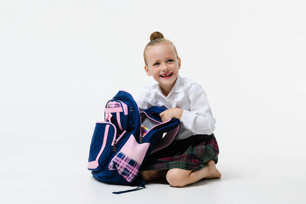 Мила дівчина в шкільній формі відкриває рюкзак для занять Ізольовані на білому тлі
. - Фото, зображення