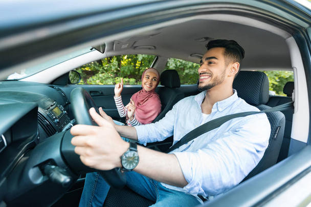 Cheerful millennial middle eastern guy driving car with lady in hijab, ride in car, enjoy music and dance while traveling, copy space. Love, relationship and family vacation, fun in road trip together - Fotoğraf, Görsel