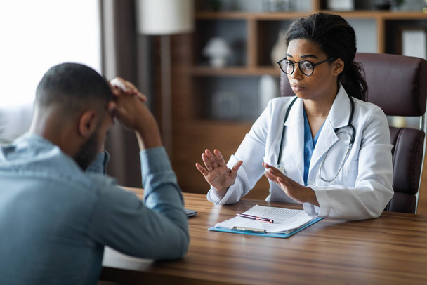 Black woman doctor consoling upset crying sick man patient, therapist supporting sad client, giving recommendations, explaining treatment plan, clinic interior, copy space. Doctor etiquette concept - Foto, Bild
