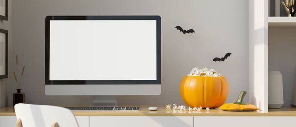 Modern home working space in Halloween theme, PC desktop computer white screen mockup, popcorn in pumpkin bucket on wood table and black bat stickers on white wall. 3d rendering, 3d illustration - Zdjęcie, obraz