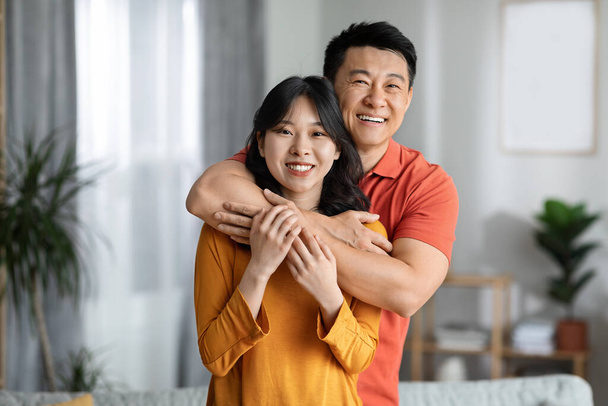 Happy asian man and woman in casual outfits cuddling in living room, hugging and smiling, posing together, enjoying weekend at home, having fun, copy space, closeup portrait - Fotoğraf, Görsel