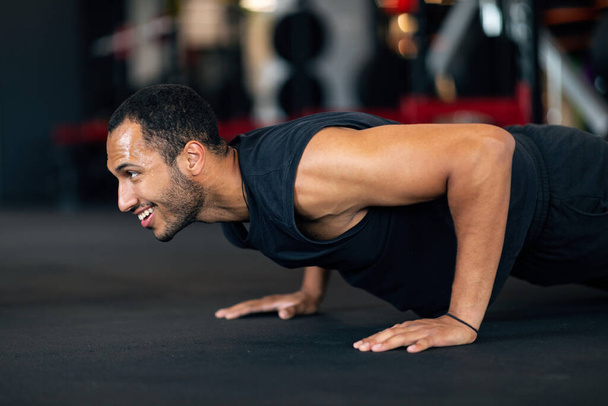 Muscular Young African American Man Doing Floor Push Up Exercise In Gym, Handsome Black Male Athele Working Out In Modern Sport Club, Making Bodybuilding Training, Closeup Shot, Side View - Foto, Imagen