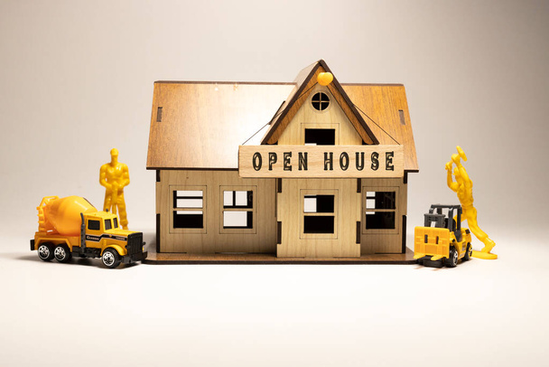 На дерев'яній поверхні написано слово "відкритий будинок". Працівники працюють над дерев'яним мініатюрним будинком на задньому плані. бізнес та фінанси
 - Фото, зображення