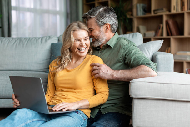 Happy Moments. Romantic Middle Aged Spouses Using Laptop And Bonding At Home, Cheerful Mature Husband And Wife Laughing And Chatting In Living Room Interior, Enjoying Spending Time Together - Foto, immagini