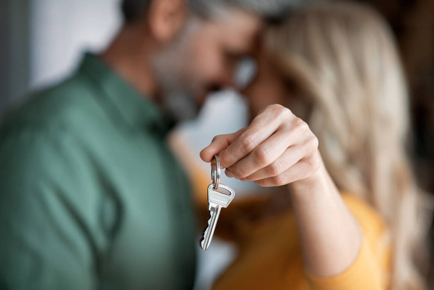 Closeup Shot Of Romantic Middle Aged Couple Holding Home Keys, Loving Mature Spouses Celebrating Moving To Their Own House, Embracing And Touching Foreheads, Cropped Image With Selective Focus - Photo, image