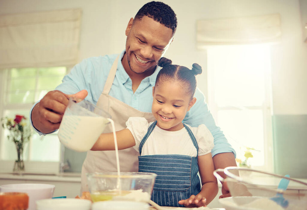 Father teaching girl to bake and make dough in a messy kitchen. Caring parent and little daughter baking together in home while pouring milk into a bowl while having fun and bonding together - Foto, afbeelding
