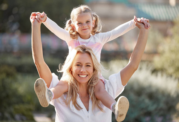 Happy mother playing with daughter on her shoulders in their backyard on a sunny day. Energetic woman play and having fun with her girl. Family bonding and laughing together on the weekend. - Foto, Imagem